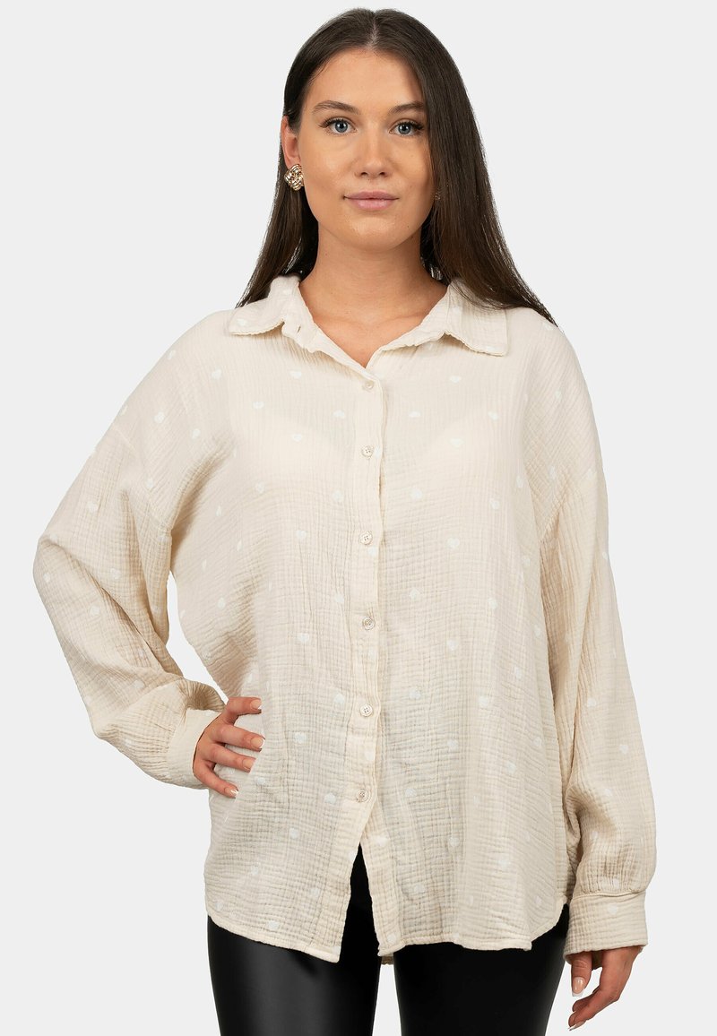 Camicia button-up beige chiaro con tessuto testurizzato, caratterizzata da motivi a forma di cuore bianchi, colletto e maniche lunghe.