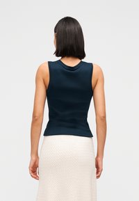 Μπλε ναυτικό εφαρμοστό τοπ με στρογγυλή λαιμόκοψη και ριγέ υφή, συνδυασμένο με ανοιχτόχρωμη φούστα με υφή που διαθέτει διακριτικό μοτίβο.