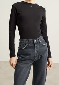 Top nero a maniche lunghe con scollatura rotonda abbinato a jeans in denim scuro a vita alta con chiusura a bottone e cuciture a contrasto.