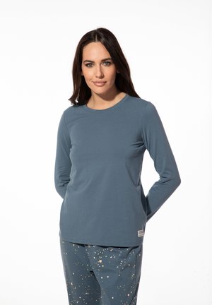 Langemouwen teal shirt van zachte stof, met een ronde hals. Gepaard met gemusterde broeken in blauw, beige en groene accenten.