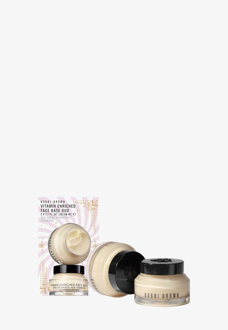 Le duo Bobbi Brown Vitamin Enriched Face Base se compose de deux pots transparents contenant une crème hydratante blanche crémeuse, avec des couvercles noirs, le tout dans une boîte décorative rose.