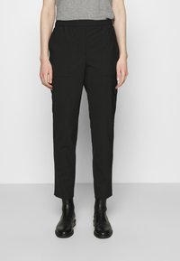 Zwarte lichtgewicht broek met een elastische tailleband, voorzien van twee zijzakken en een taps toelopende pasvorm. Gecombineerd met zwarte enkellaarzen.