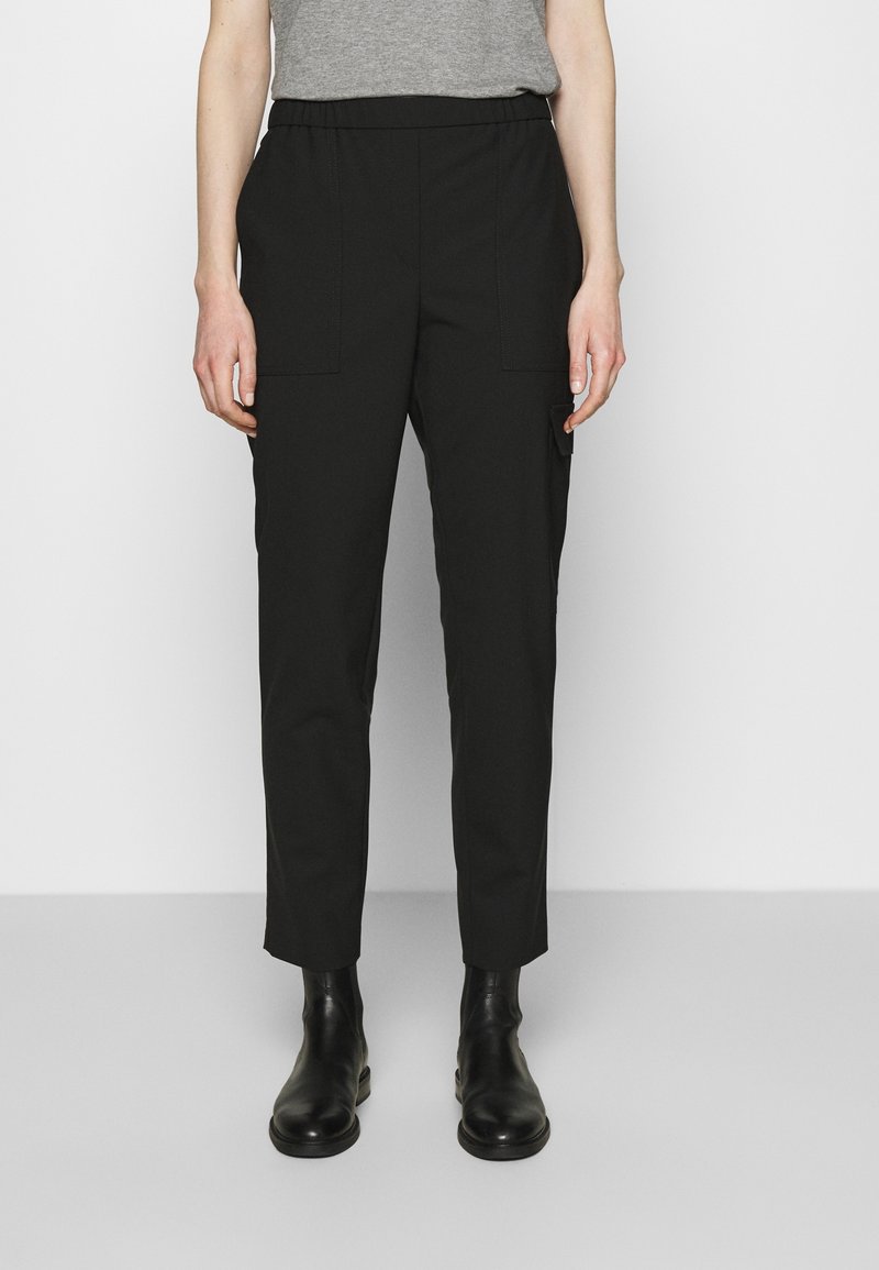 Zwarte lichtgewicht broek met een elastische tailleband, voorzien van twee zijzakken en een taps toelopende pasvorm. Gecombineerd met zwarte enkellaarzen.