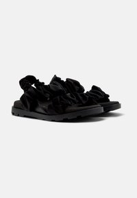 Svarta platta sandaler med en strukturerad svart sula, som har en samlad tygovandel för ett rynkat utseende. Öppen design utan ytterligare beslag.