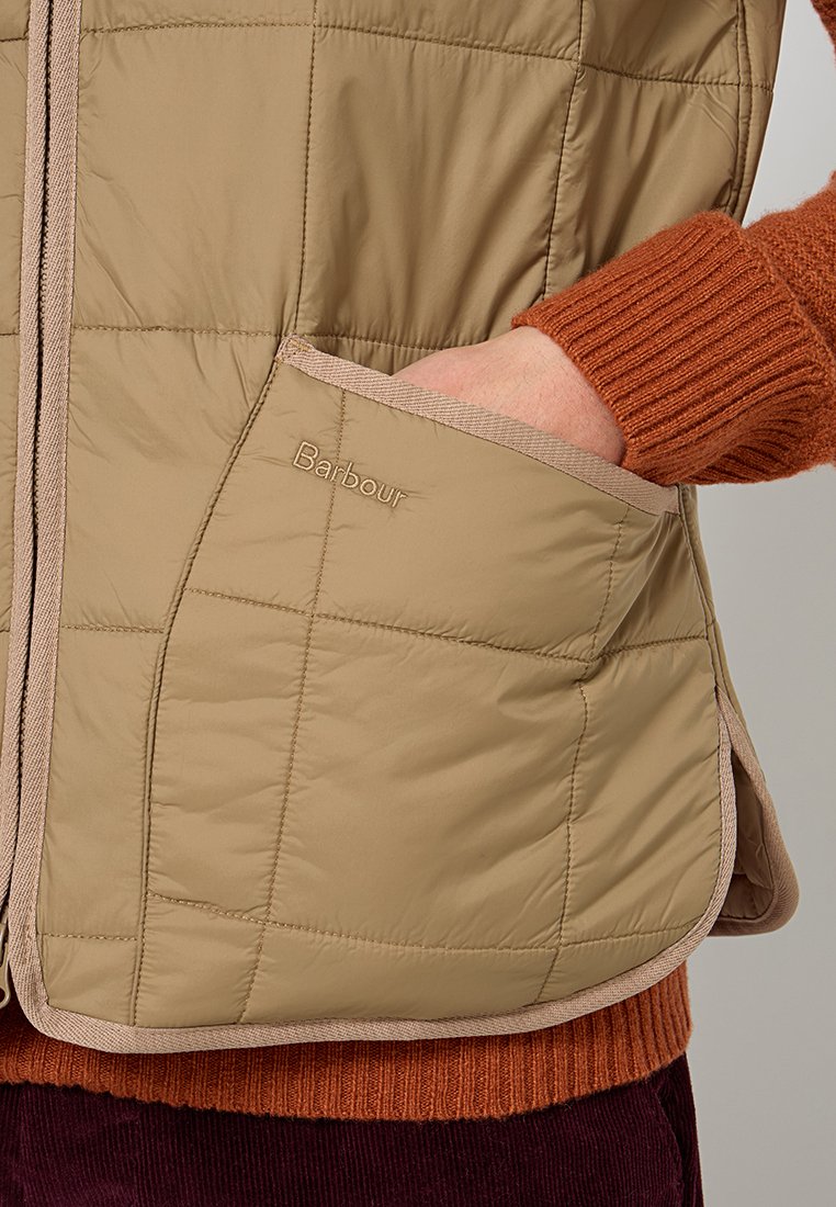 Gilet puffer beige con quadrati cuciti, rifinitura a contrasto e tasca frontale con logo "Barbour". Tessuto testurizzato, design di lunghezza media.