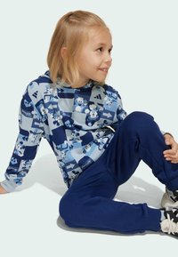 Hoodie w jasnoniebieskim kolorze z wzorem z kreskówkami, w połączeniu z ciemnoniebieskimi spodniami dresowymi. Materiał wydaje się miękki i komfortowy.