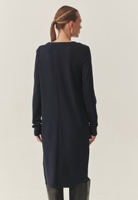 Tengerészkék hosszú ujjú ruha egyenes szabással, kerek nyakkal, keskeny mandzsettákkal és középen hátulvarrással, puha anyagból készült.