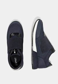 Baskets bleu marine avec sangle élastique, détails en cuir verni noir, tige texturée et semelle extérieure blanche. Présentent une silhouette basse et une forme arrondie au niveau des orteils.