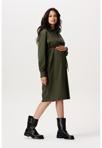Olivgrünes Hemdblusenkleid mit langen Ärmeln und gebundenem Taillenbereich, kombiniert mit schwarzen Leder-Ankleboots mit dekorativen Schnallen.