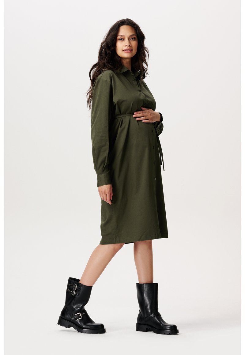 Olivgrünes Hemdblusenkleid mit langen Ärmeln und gebundenem Taillenbereich, kombiniert mit schwarzen Leder-Ankleboots mit dekorativen Schnallen.