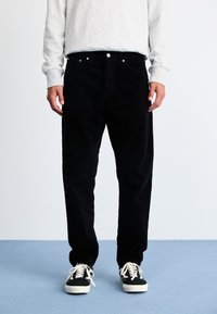 Zwart corduroy broek met een rechte pijpdesign, voorzien van een knoopsluiting, voorzakken en gecombineerd met zwart-witte sneakers.