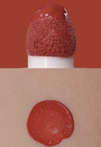 Lápiz labial líquido rojo en la punta de un aplicador aterciopelado, con una muestra circular en la piel debajo que muestra una textura suave y uniforme.