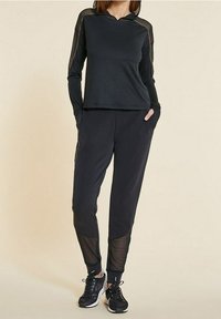 Black athletic outfit featuring a long-sleeve hooded top with mesh accents and matching tapered pants with mesh details, paired with black sneakers.