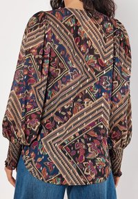 Blouse à motif floral avec un fond sombre, des manches bouffantes et des poignets smockés ; les tissus ont une texture lisse et légère.