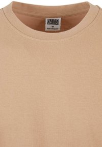 Lichtbeige katoenen t-shirt met een ronde hals. Kenmerken een gelabeld label binnenin met de tekst "URBAN CLASSICS, Made in Bangladesh." Zachte textuur.