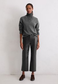 Grauer Strick-Turtleneck-Pullover mit V-Ausschnitt, kombiniert mit hochtaillierten schwarzen weiten Lederhosen und braunen Wildleder-Slippern.