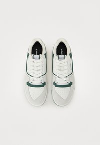 Hvite og grå semskede sneakers med grønne detaljer, som har perforert tå, hvite snørebånd og merking på tungen og siden.