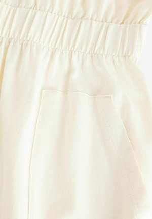 Beige bomullstyg med elastisk midjereså. Slät textur, minimal sömdetalj och avslappnad passform.