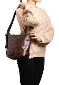 Borsa a spalla in pelle marrone con finitura lucida. Presenta una tracolla larga e regolabile e accessori in metallo. Forma rettangolare con fondo piatto.