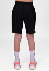 Schwarze Sportshorts mit einem elastischen Bund, Seitentaschen und einem leichten Stoff. Getragen mit weißen Socken und mehrfarbigen Turnschuhen.