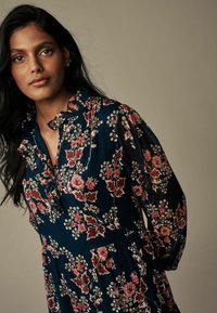Floral dress with navy background, featuring pink roses and leaves, ruffled collar, and long puffed sleeves. Lightweight fabric with a flowing design.