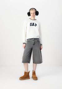 Valge kampsun, millel on merevaigu värvi "GAP" logo, hallid denimplaadid ja pruuni suede'ist säärebotased, mille sees on lamba karv. Mustad kõrvakatteid t�äiendavad välimuse.