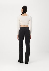 Jeans pretos com boca de sino, cintura alta e design de cinco bolsos. Usados com uma blusa justa de manga longa e de cor clara. Textura de tecido suave.