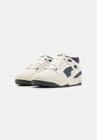 Sneaker atletiche bianche e blu navy con parte superiore in suede e tessuto, design con lacci, linguetta imbottita e suola in gomma testurizzata. Dettagli di cucitura a contrasto.