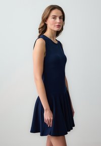 Robe sans manches bleu marine avec un corsage ajusté et une jupe évasée. Fabriquée en tissu lisse avec une couleur unie et sans motifs visibles.