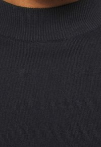 Mörkblå stickad tröja med ribbad struktur och hög hals. Materialet verkar mjukt och stretchigt, passar bra för avslappnad användning.