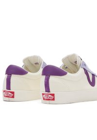 Sneaker bianche in tela con dettagli in pelle viola e linguetta, suola in gomma piatta e etichetta rossa sul tallone. Vista posteriore.