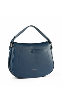 Bolso de hombro de cuero azul con forma redondeada, textura suave, solapa frontal y un detalle de logo dorado. Cuenta con una correa corta y ajustable.