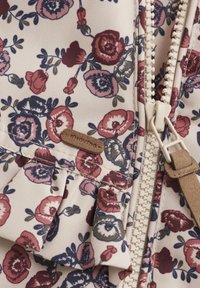 Bloemige zip-up jas met een roomkleurige achtergrond, voorzien van rode en blauwe bloemen, een ruchesdetail en een beige stoffen label. De rits is wit.