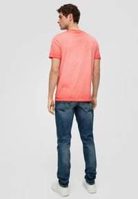 Camiseta de manga corta color coral con cuello redondo, combinada con jeans azules. La tela parece suave y ligeramente texturizada. Ajuste y estilo casual.