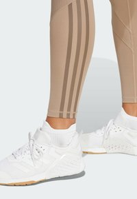 Beige atletiske leggings med brune vertikale striber og tekstureret overdel; parret med hvide sneakers med mesh og gummidetaljer.