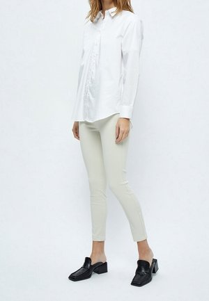 Bílá košile s dlouhým rukávem a knoflíkovou légou, spárovaná s lehkými béžovými slim kalhotami a černými muly se čtveratou špičkou a masivním podpatkem.