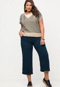 Top de punto con un patrón ondulado en beige y azul marino, combinado con culottes sueltos de color azul oscuro. La modelo lleva zapatos negros y una pulsera.