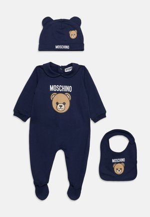 Granatowy zestaw niemowlęcy z kombinezonem z długim rękawem i stopami, czapka z uszami misia oraz śliniak, wszystkie z twarzą misia pluszowego i logo Moschino.