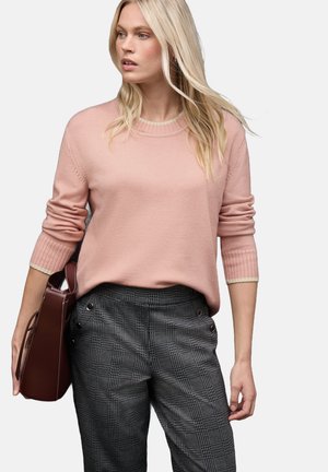 Ljust rosa, stickad tröja med rund halsringning och ribbade ärmslut, kombinerad med svart-vita rutiga, högmidjade byxor. Brun handväska som accent.