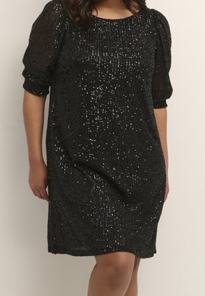 Woman wearing a black, knee-length dress with puff sleeves and all-over small sequins creating a sparkling effect.