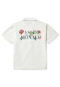 Polo shirt bianca a maniche corte con "PAS DE MONACO" in caratteri scuri e decorazioni floreali rosse e verdi sul retro.