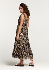 Rochie maxi cu model floral în tonuri de negru și bej, cu bretele volanate, bust ajustat și tiv evazat. Asortată cu sandale cu curele.