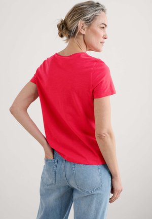 Red cotton t-shirt with short sleeves and a rounded neckline, featuring a relaxed fit and a smooth texture, paired with light blue jeans.