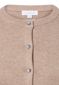 Cardigan beige en tissu tricoté texturé. Présente un col rond et cinq boutons argentés sur le devant. L'étiquette indique une taille S.