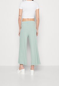 Lichtgroene, wijde broek met een gestructureerde stof en een elastische tailleband, gecombineerd met een aansluitende witte crop top en witte block-heeled sandalen.