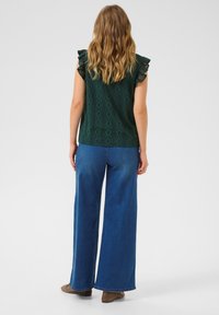 Haut à motifs verts avec des manches volantées, associé à un jean en denim bleu à larges jambes. Le tissu semble léger ; design décontracté.