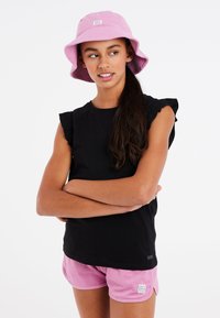 Sort t-shirt med flæser på ærmerne, kombineret med lyserøde håndklædeshorts og en matchende lyserød bøttehat med et logo-patch.