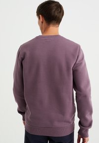 Lila fleece-tröja med ribbstickade muddar och nederkant, rund halsringning, mjuk textur och en liten etikettdetalj på baksidan.