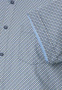 Blauw gemarmerd shirt met een geometrisch ontwerp in verschillende blauwtinten, beige en marineblauw; inclusief knopen en een borstzakdetail.