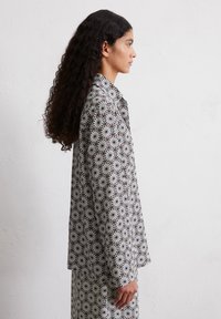 Gemusterte Jacke mit einem schwarz-weißen kreisförmigen Design, aus leichtem Material gefertigt, mit mittellanger Schnittform und langen Ärmeln.